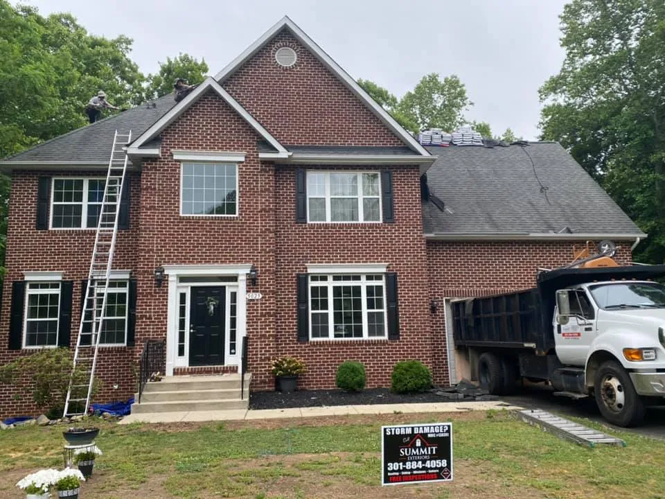 Brick colonial in Waldorf, MD with Summit Exteriors dump truck and ladders during a roof replacement with Storm Damage yard sign