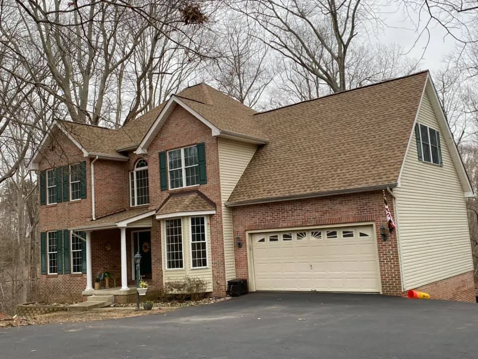 Brick colonial in Owings, MD with green shutters and a new tan architectural shingle roof installed by Summit Exteriors