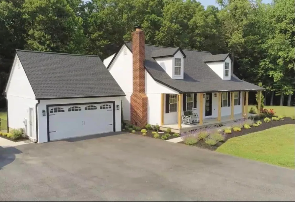 White Cape Cod home with detached two-car garage in Charlotte Hall, MD featuring a new charcoal architectural shingle roof and brick chimney