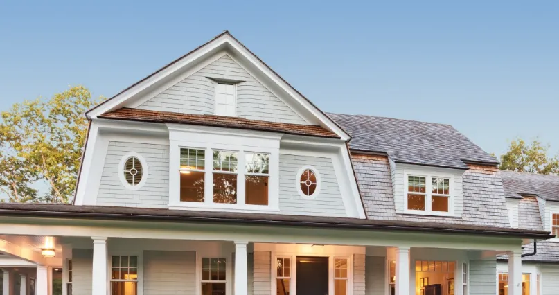 Gambrel-roof Leonardtown, MD home with cedar shake-style architectural shingles, oval windows and a covered front porch for a roof replacement project in Leonardtown, MD
