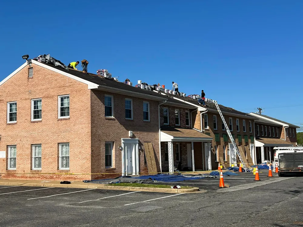 Summit Exteriors crew replacing the roof of a long brick commercial townhome row in Waldorf, MD with safety cones and tarps