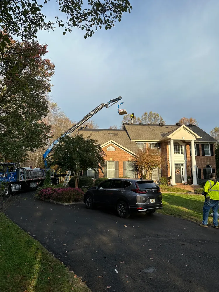 Summit Exteriors crew using a boom-lift crane to load shingles onto a large brick colonial roof in Hughesville, MD — roof replacement project in Hughesville, MD by Summit Exteriors