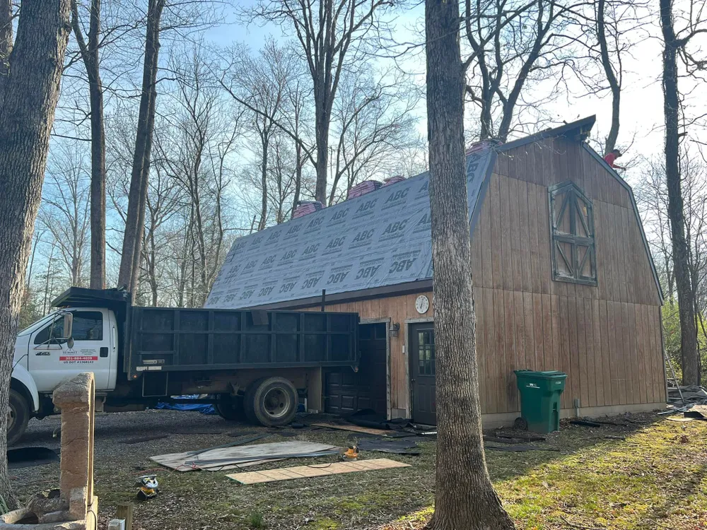 Summit Exteriors dump truck parked next to a wooden gambrel-roof barn in Hughesville, MD getting a new architectural shingle roof