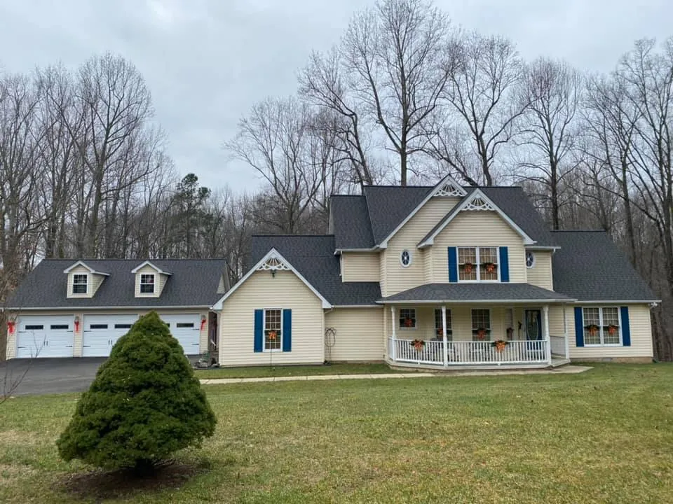 Yellow farmhouse with attached three-car garage in Mechanicsville, MD featuring a new charcoal architectural shingle roof and wraparound porch