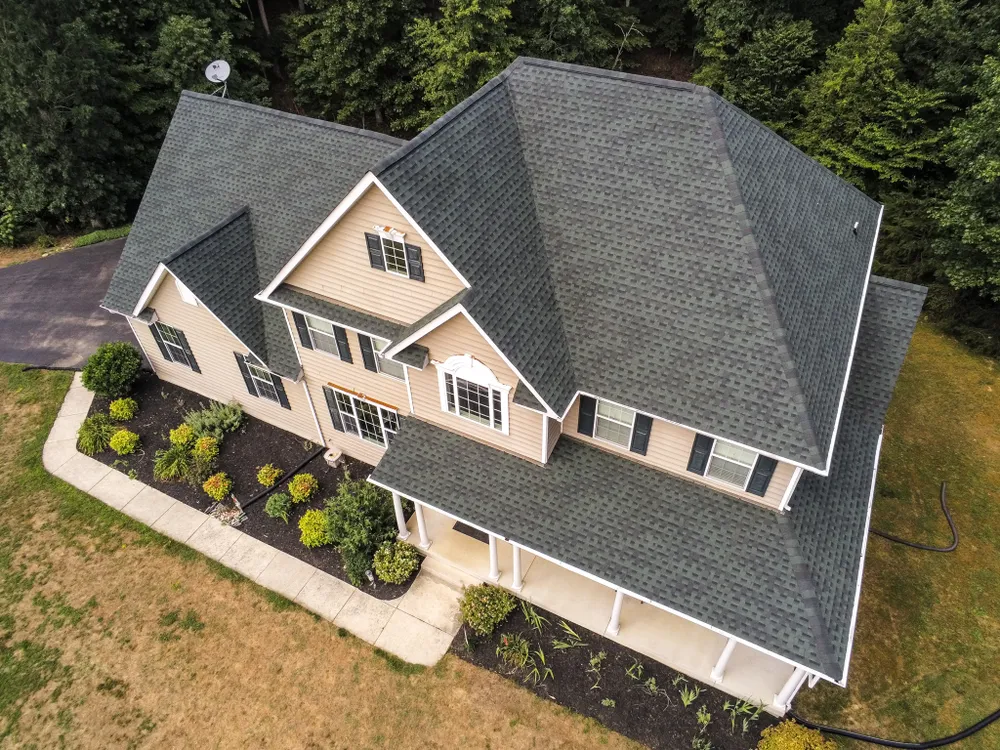 Tan colonial home in Chesapeake Beach, MD with new green architectural shingles and a covered front porch