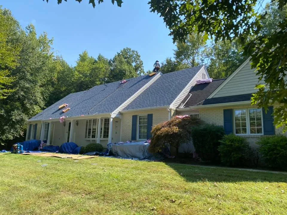Brick rancher in Bryans Road, MD with tarps protecting landscaping and Summit Exteriors crew installing new architectural shingles