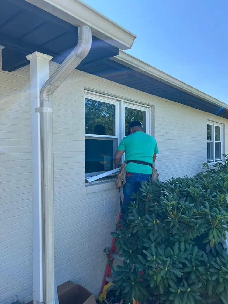 Summit Exteriors installer replacing a window on a white brick rancher with new white aluminum gutters in Lexington Park, MD
